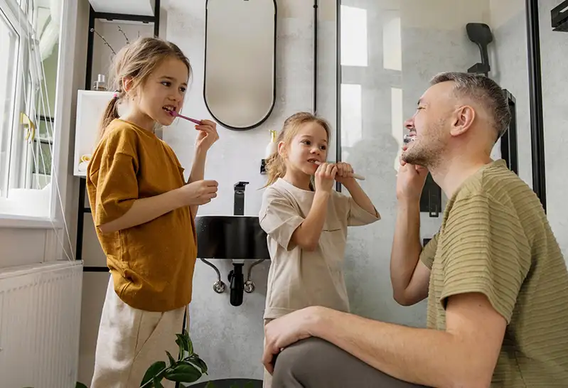 A father shows his children how to brush their teeth in the bathroom.