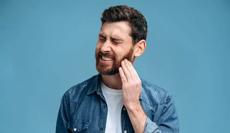A man winces and touches his cheek in pain from cavities.