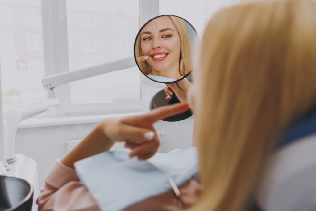 A female dental patient smiles while looking at her teeth in a mirror.