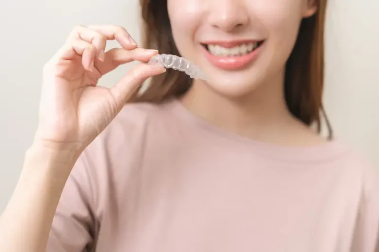 A smiling dental patient holds a transparent aligner from Invisalign.