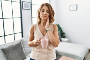 A woman rubs her cheek in discomfort, representing one of the myths about dental implants and how they'll lead to pain.