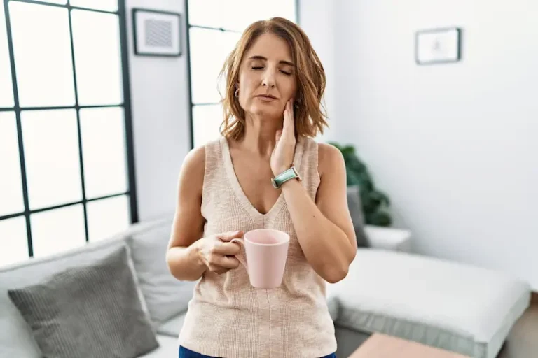 A woman rubs her cheek in discomfort, representing one of the myths about dental implants and how they'll lead to pain.