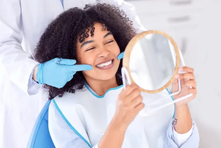 A smiling patient lying on a dental chair uses a mirror to look at her teeth whitening results.