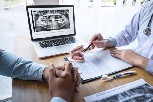 Man asking are you sedated for dental implants during a dental consultation and the dentist explaining the process through showing him a prop of teeth within a mouth.