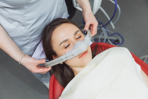 Woman receiving sedation through inhalation mask for a dental implant surgery by a dentist.