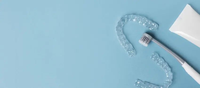 Clear Invisalign® aligner trays are beside a toothbrush and toothpaste which represent a proper cleaning and maintenance routine from The Foleck Center.