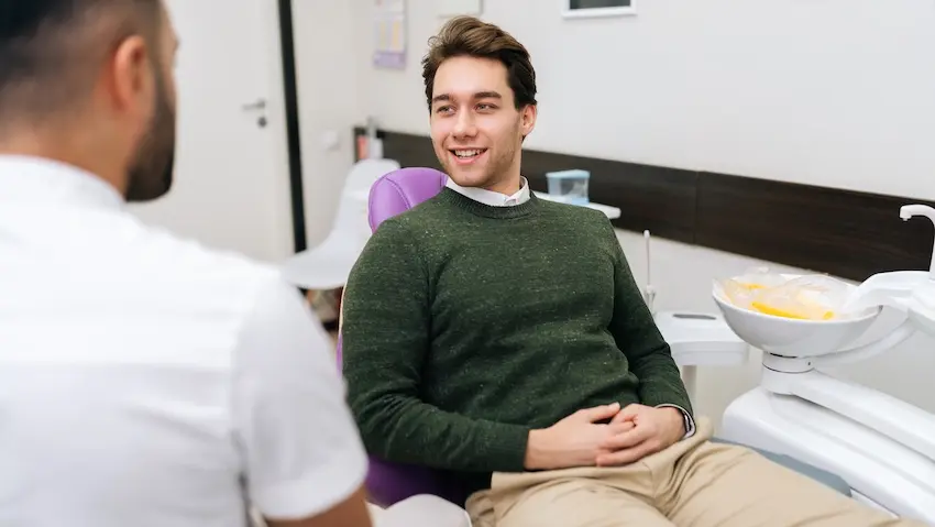 A smiling male patient in a cactus green sweater is consulting with a dentist about Invisalign® treatment plan and progress evaluation at The Foleck Center in Virginia.