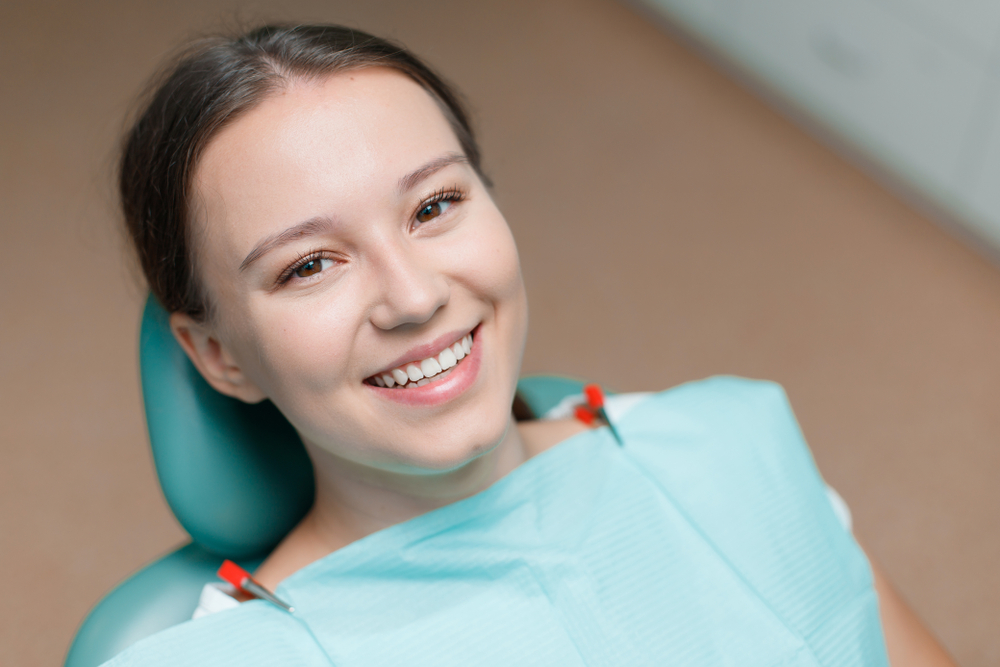 Beautiful young woman in dental chair. Smiling and satisfied patient at dentist's office after treatment. Healthy teeth, dental care concept.