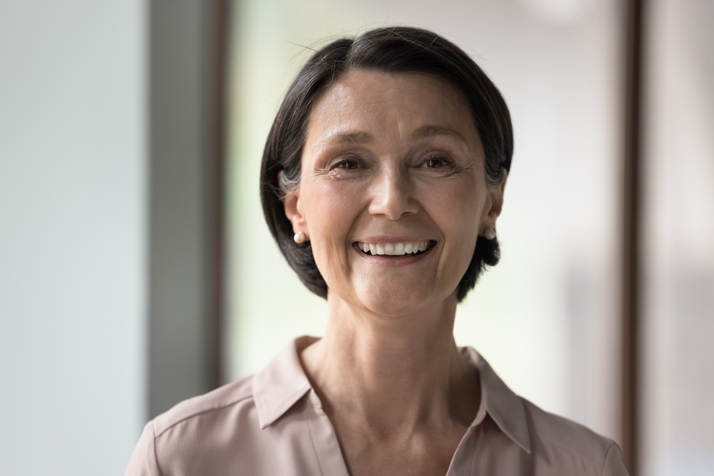 Close up head shot beautiful brunette mature businesswoman look at camera pose indoors, having wide pretty smile, advertise dental services. Happy aged teacher, company boss, older executive portrait