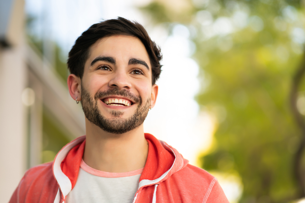 Straight smile after Invisalign in Norfolk, VA, The Foleck Center Young man smiling broadly outdoors with straight, healthy teeth after Invisalign treatment at The Foleck Center, Norfolk, VA