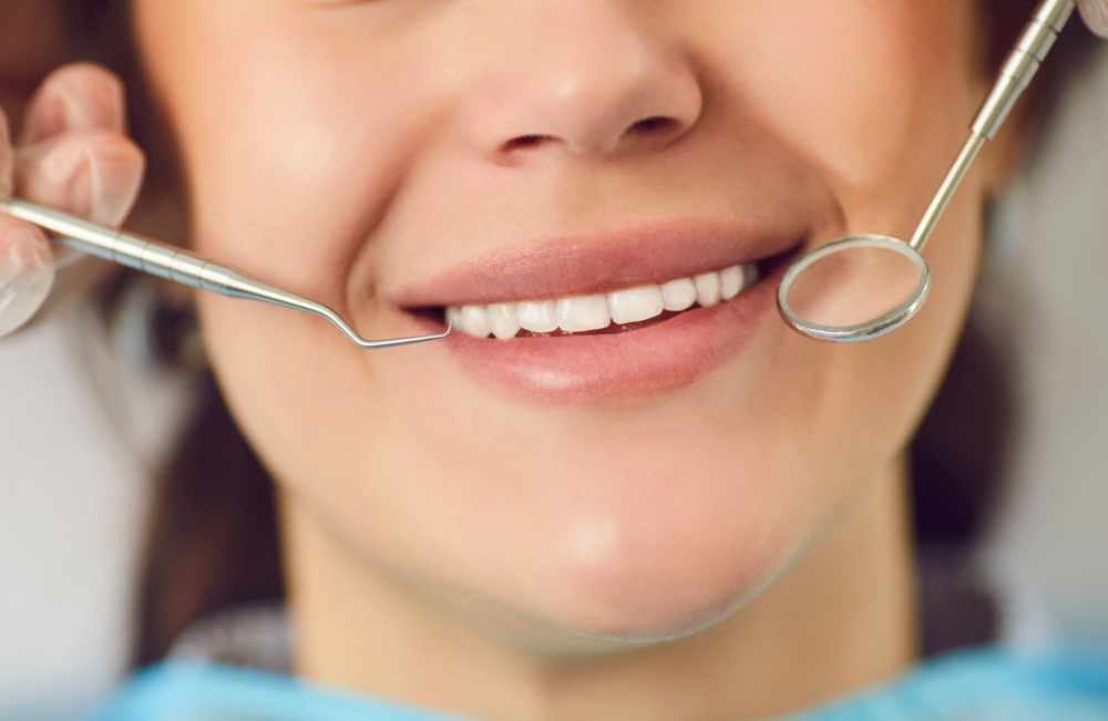 Close up portrait of a woman patient smiling mouth being examined by a dentist doctor using instruments during a dental checkup in the hospital office. Focus on teeth and oral care.
