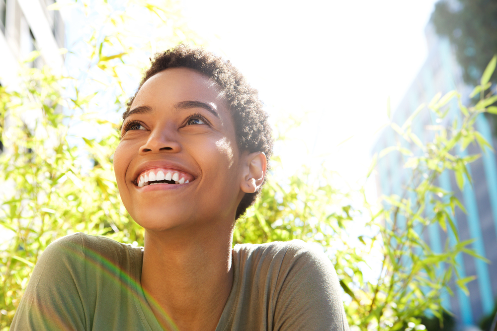 Woman smiling brightly outdoors in natural sunlight, representing the healthy smiles achieved through restorative dentistry in the Hampton Roads community 