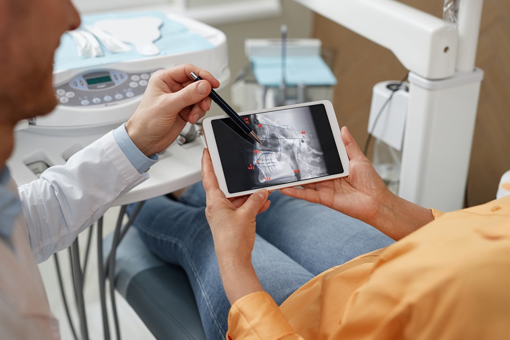 Dentist pointing at a tooth X-ray on a tablet during a patient consultation 