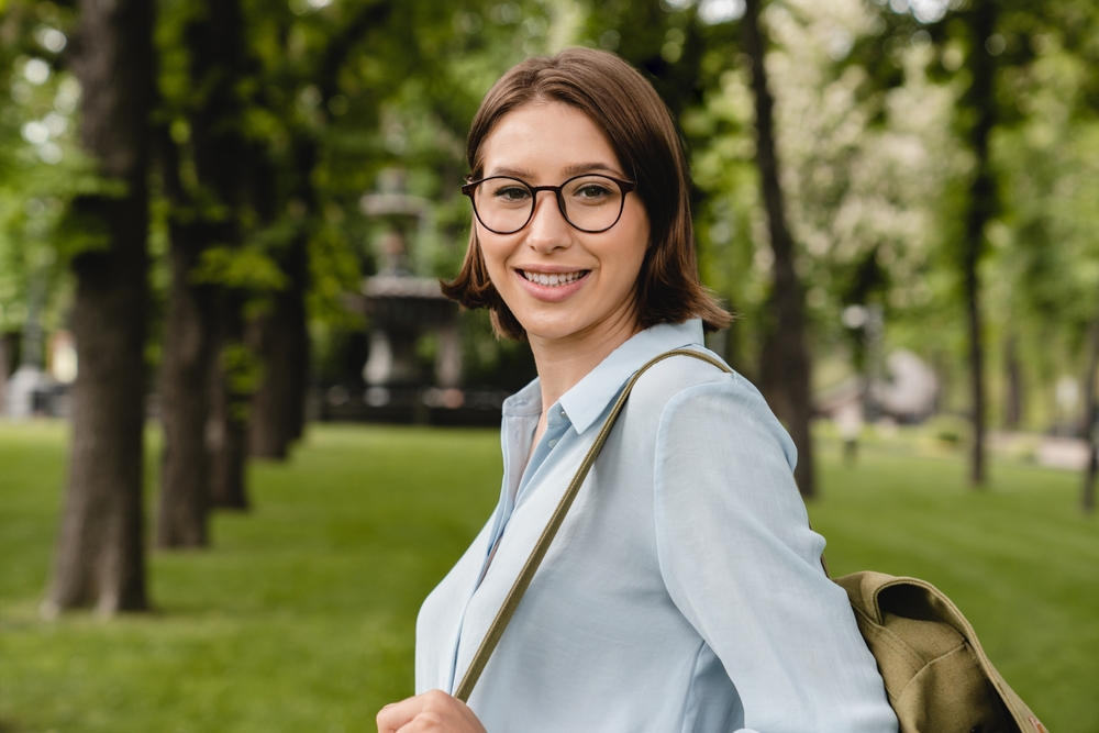 Confident young female student teacher business woman tutor consultant adviser in formal clothes outfit walking in the city park, relaxing after meeting, working remotely as a freelancer outdoors
