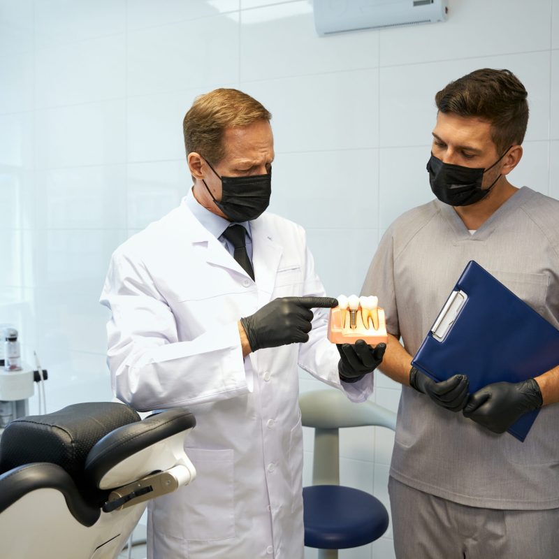 A certified dental technician talks with a dentist about a tooth restoration using a model.