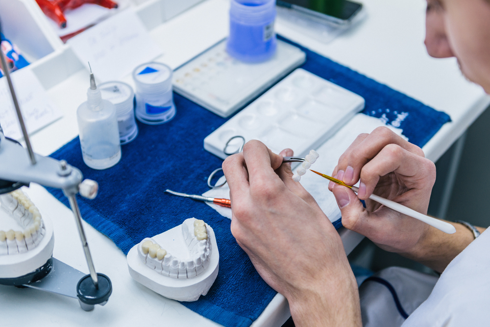 Dental lab technician crafting a custom restoration using a tooth colored shade guide at The Foleck Center's in-house dental lab 