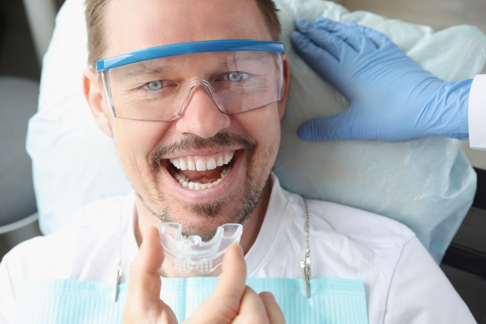 Night Guard Fitting: Virginia Beach Dental Office Smiling man holding a night guard fitted during a full-mouth reconstruction visit in Virginia Beach
