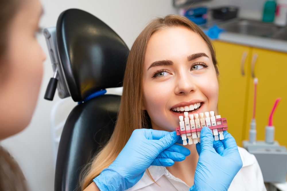 Dentist selects a shade of teeth whitening using shade guide to young patient with perfect smile