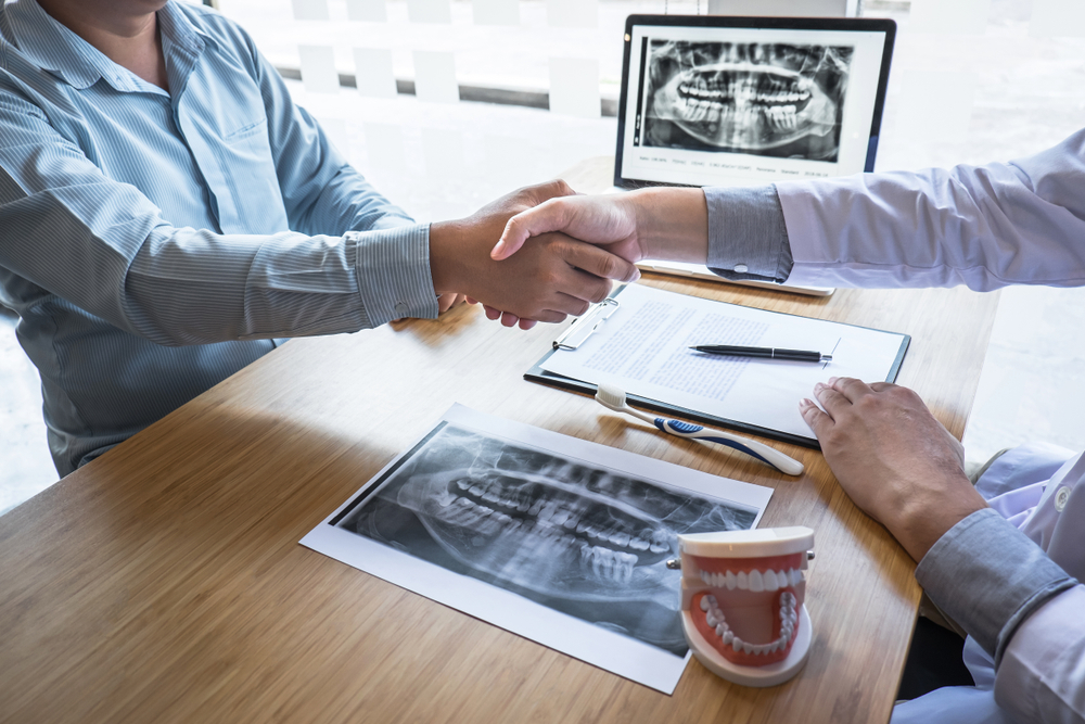 Dentist and patient shaking hands over dental x-rays during a cosmetic dentistry consultation in Virginia Beach 