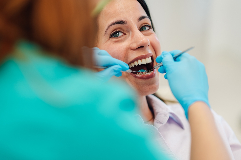 Dentist wearing blue gloves using dental tools while examining patient teeth during dental checkup in clinic, healthcare and dentistry concept
