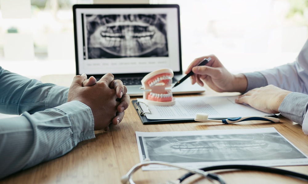 Laptop displaying a panoramic dental X-ray next to a dentures model and printed X-ray images 