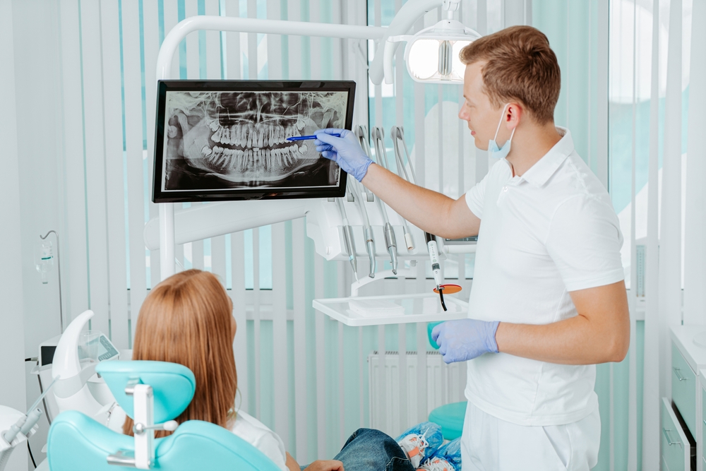 Dentist pointing to a panoramic X-ray on screen while reviewing it with a seated patient