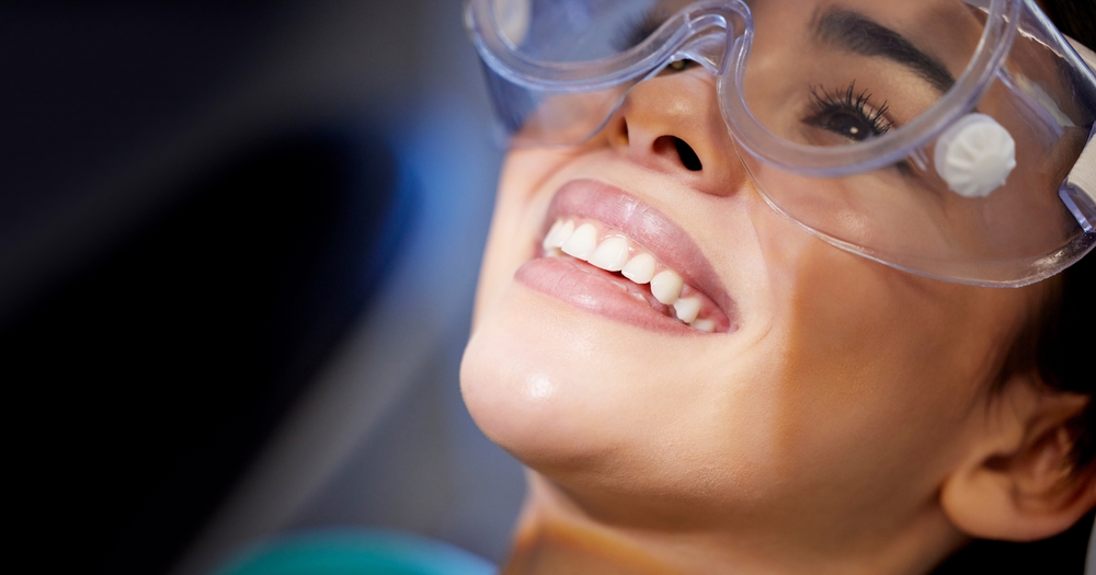 Face, goggles and smile with woman at dentist for oral hygiene or dental care appointment closeup. Checkup, healthcare and medical with happy patient in chair at clinic for mouth cleaning or exam