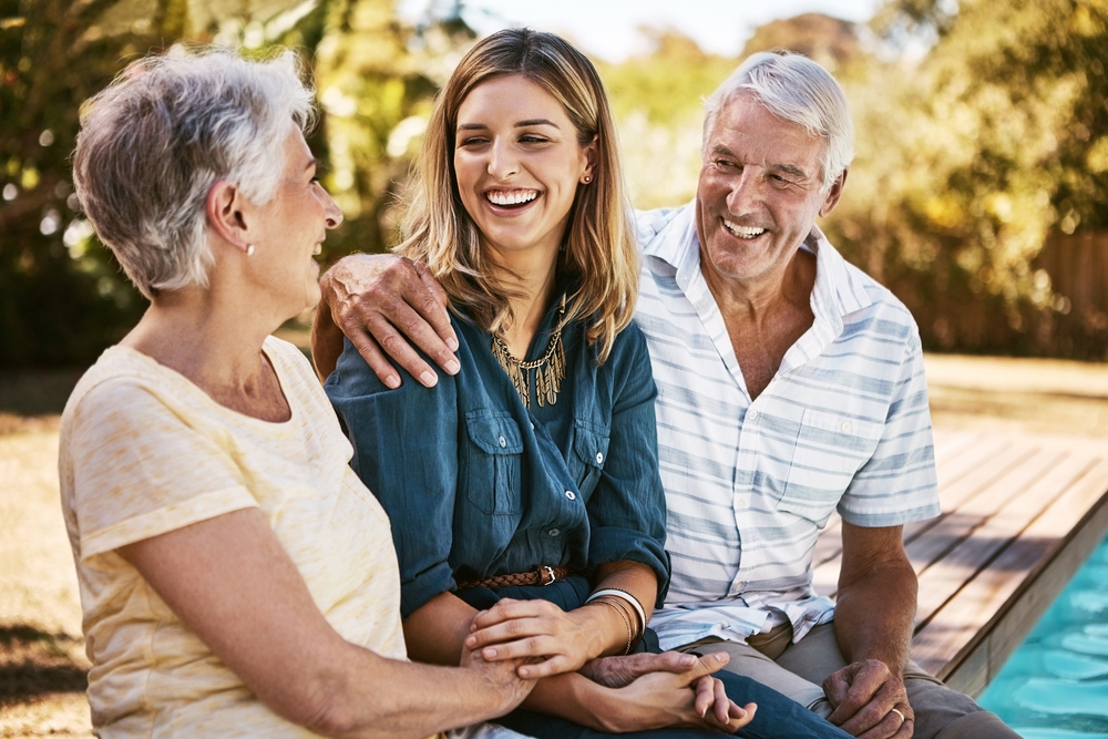 Adult woman laughing with her elderly parents outdoors, reflecting confidence and quality of life after dental implant treatment at The Foleck Center, Norfolk, VA 