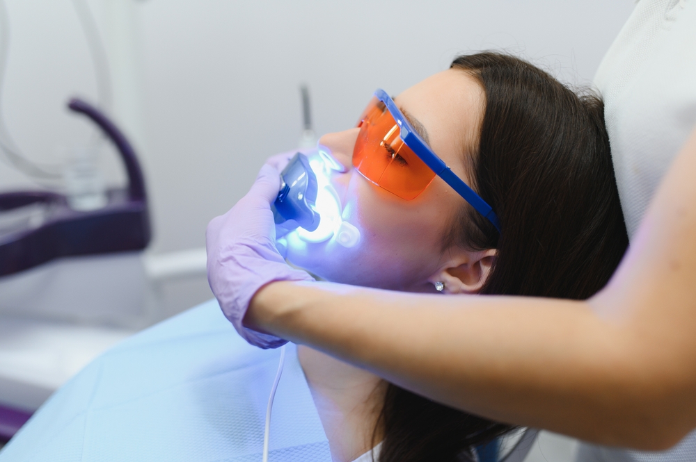 Girl patient in the dental clinic. Teeth whitening UV lamp with photopolymer composition