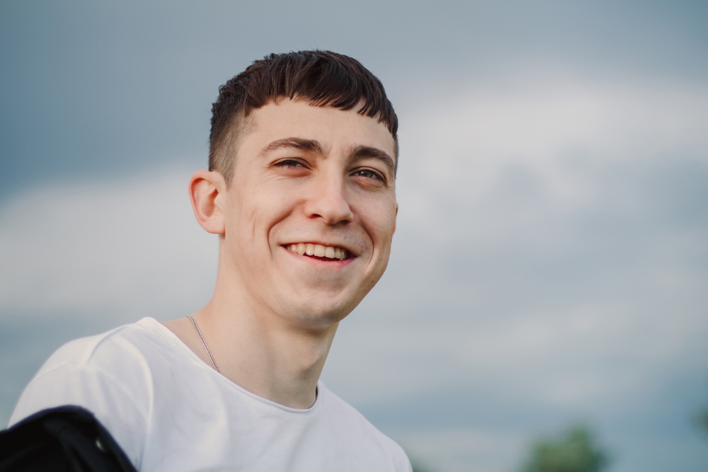Handsome man in a white T-shirt laughs. Outdoors portrait against the background of the sky. Wide smile with teeth.