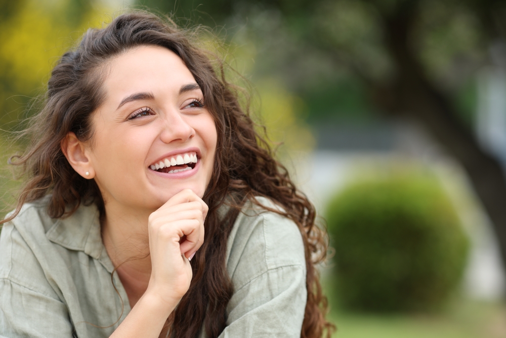 Happy beauty woman laughing sitting in a park looking at side