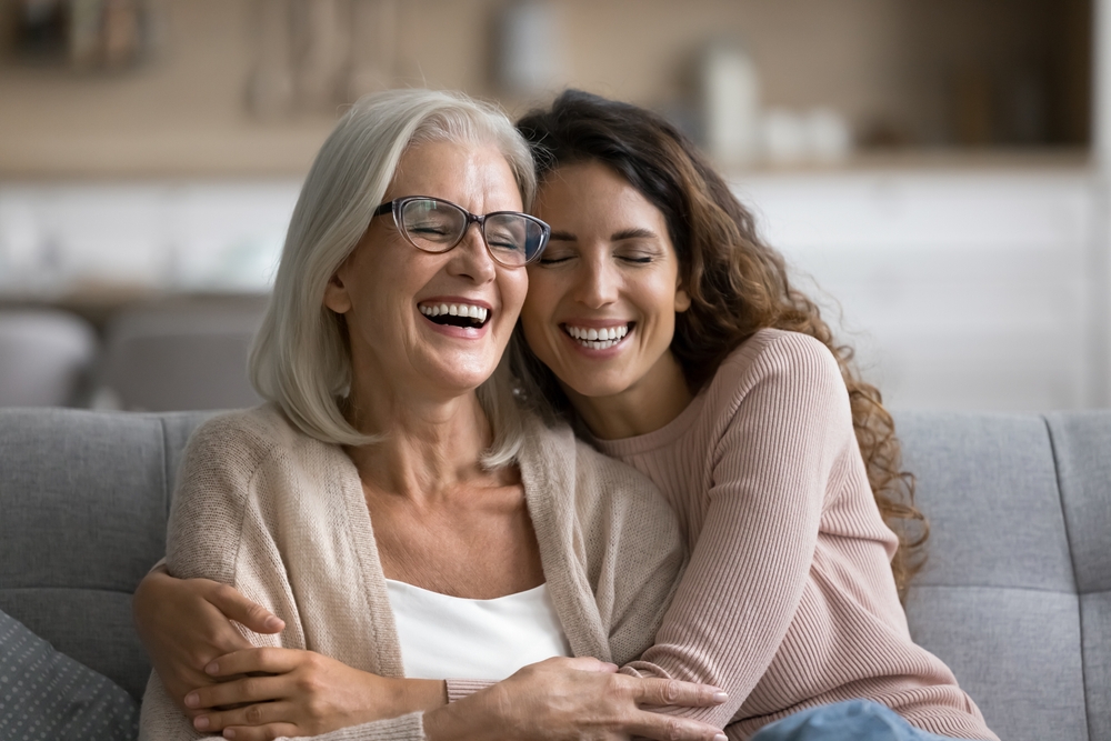 Two women laughing together while embracing on a couch 