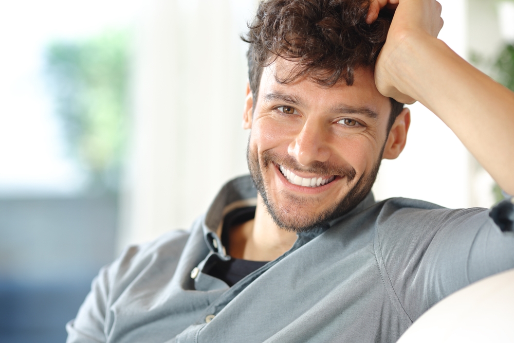 Happy handsome man is looking at camera sitting on a couch at home