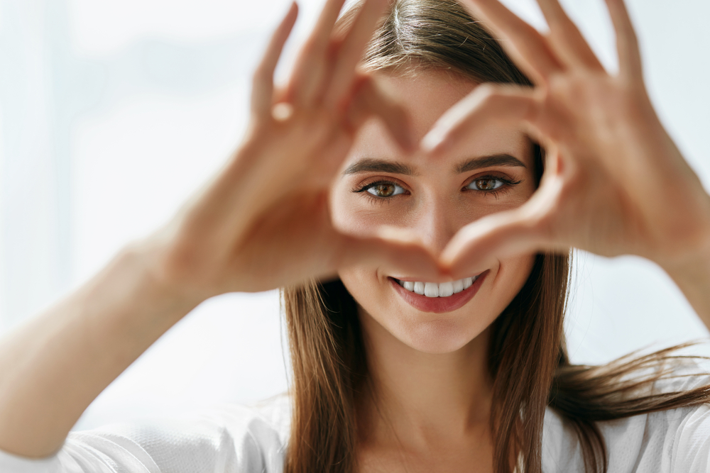 Woman making a heart shape with her hands near her smiling face 