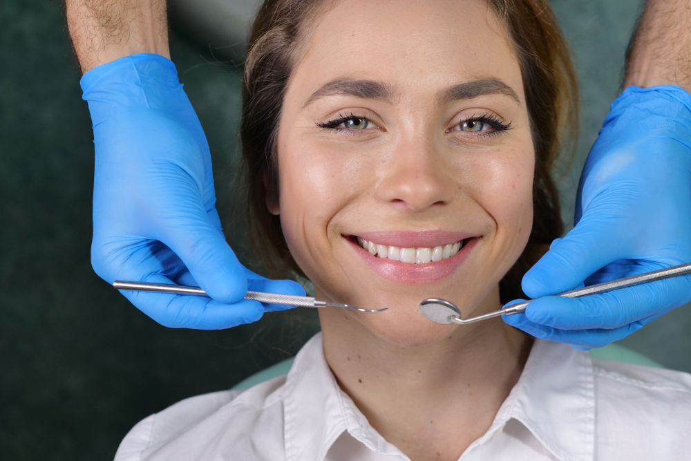 In a professional practice, a dentist checks the dentition of the patient, and she is happy with the visit, smiling, showing the perfect white teeth. Concept of: dentists, healthcare, perfect smile.