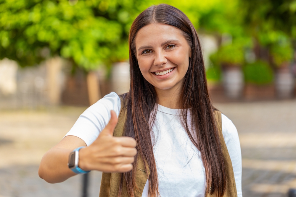Like. Happy woman raises thumbs up agrees with something or gives positive reply recommends advertisement likes good idea feedback, celebrating success victory. Girl standing on urban city street.