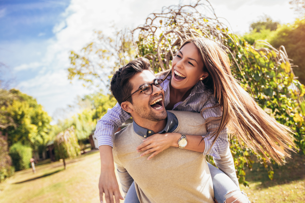 Couple laughing together outdoors, reflecting the confident smiles patients enjoy in the Norfolk community 