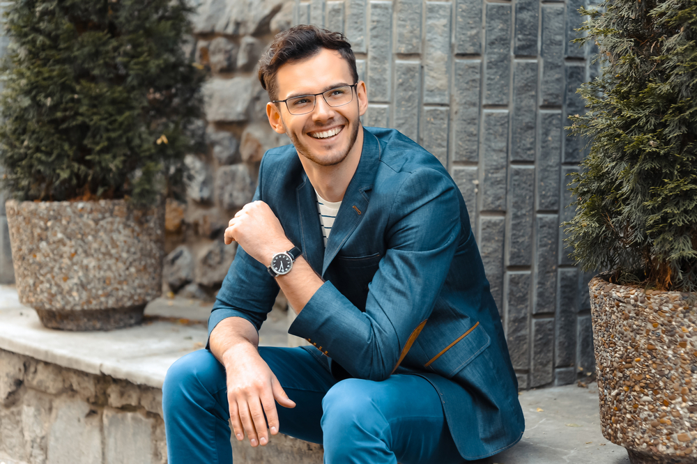 Man in a tailored blue suit smiling confidently outdoors, representing the healthy smiles achieved in the Norfolk community 