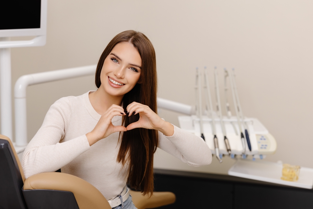 Patient is smiling and gesturing hands heart in dentist office.