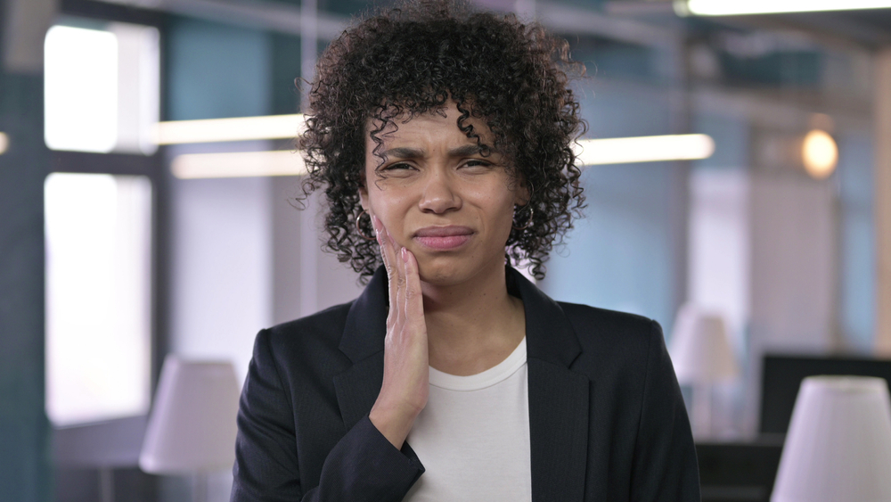 Gum pain, a sign of advancing gum disease Woman in a blazer wincing and touching her cheek in pain