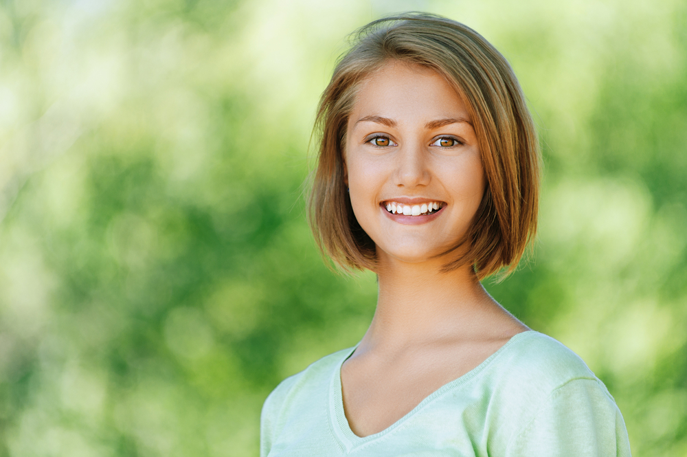Portrait of smiling beautiful young woman close up, against background of summer green park.