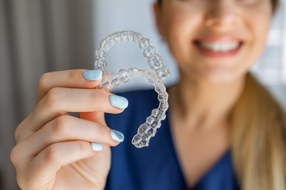 Invisalign aligners: clear alternative to braces in Norfolk Hands holding two clear Invisalign aligners with a smiling person blurred in the background
