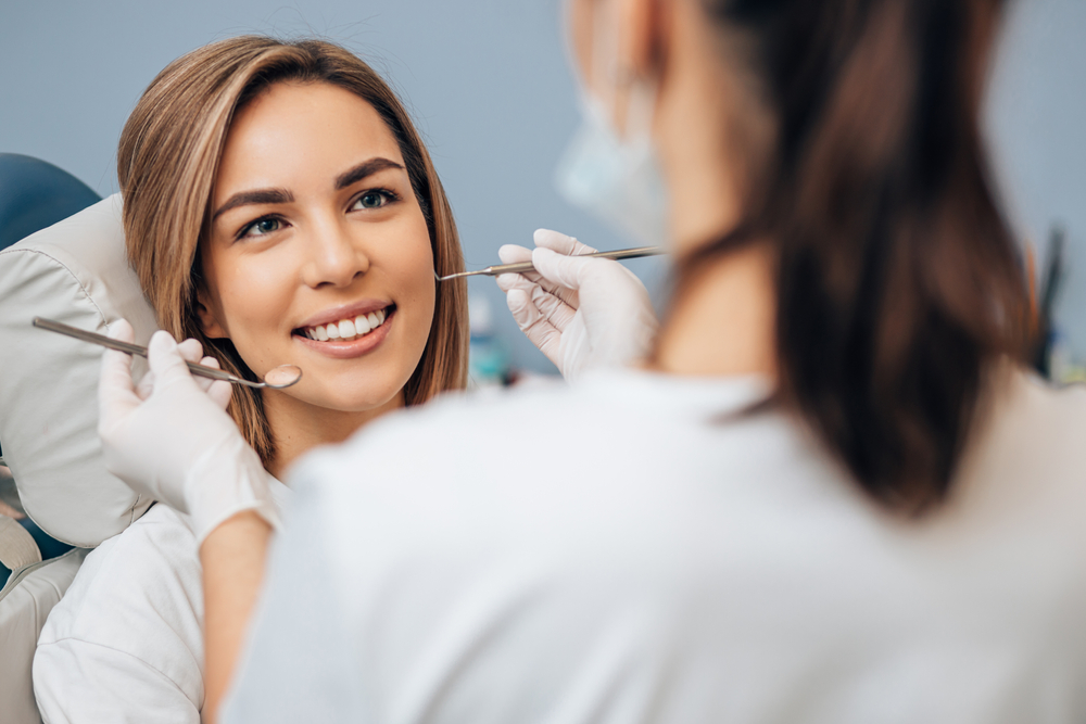 Dentist examining a smiling patient's teeth with a mirror and explorer 