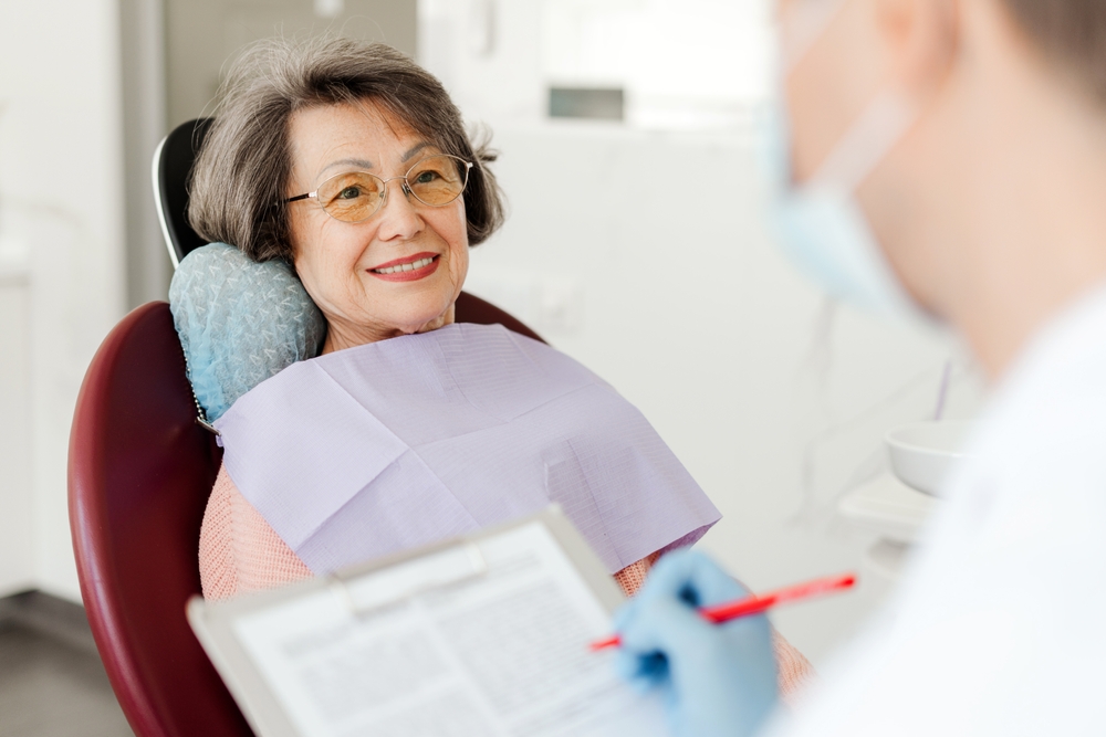 Smiling, beautiful senior woman sitting in dental chair on visit to dentist, talking in modern dentistry. Concept of dental care