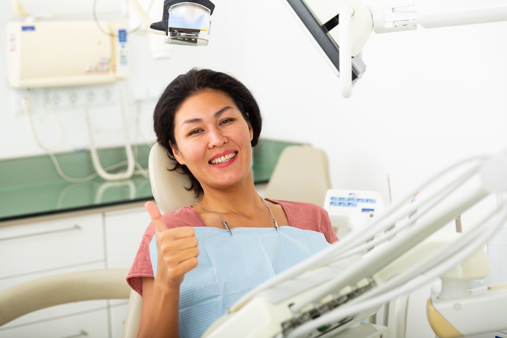 Smiling female patient showing thumb up after dental treatment in clinic