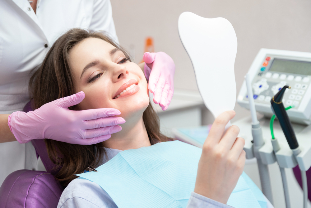 Patient admiring her smile in a hand mirror during a restorative dentistry visit in Hampton Roads 