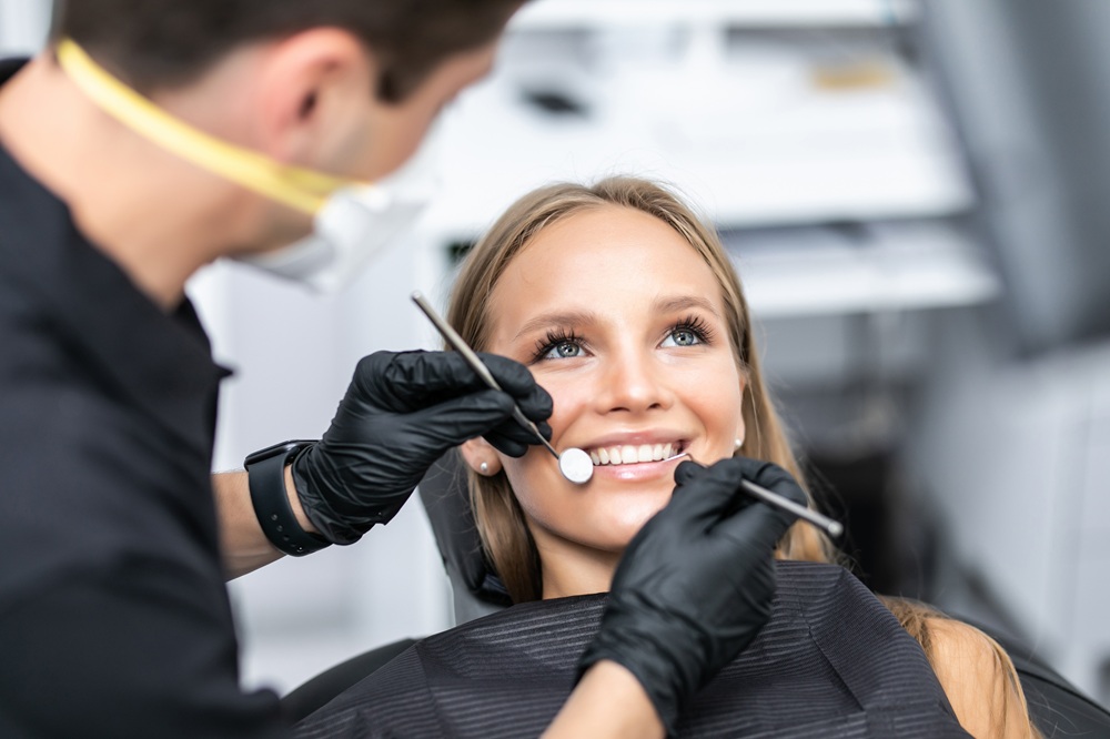 Dentist in black gloves examining a smiling patient's teeth with a mirror and explorer tool