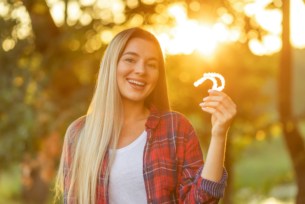 Invisalign clear aligners in Norfolk, VA, The Foleck Center Young woman smiling while holding Invisalign clear aligners outdoors at The Foleck Center, Norfolk, VA