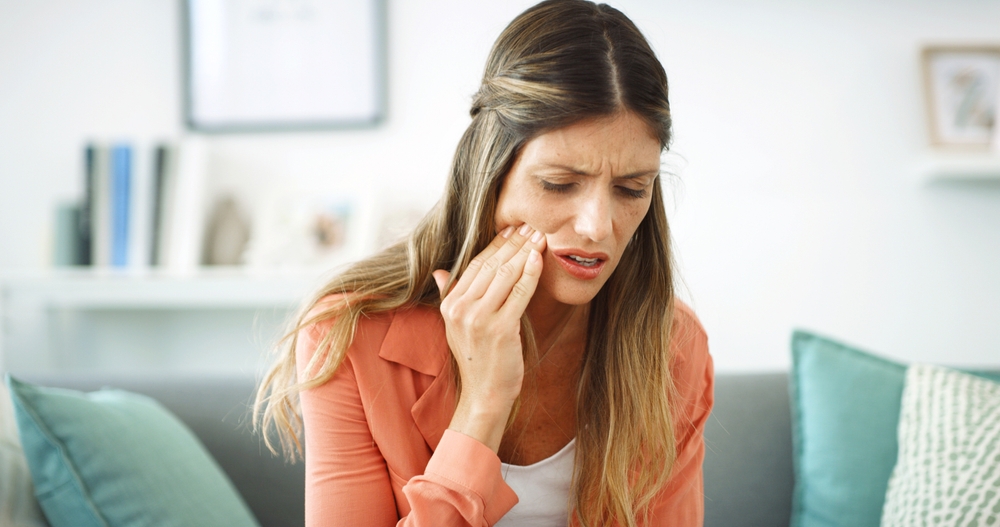 Woman, touch and cheek with toothache at house with cavity, dental problem and gum infection.