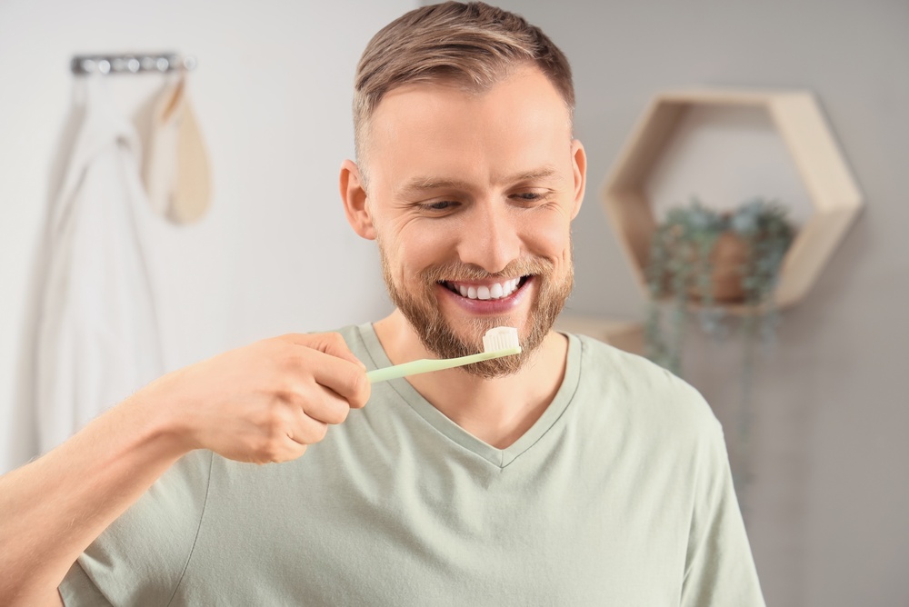 Good oral hygiene helps prevent gingivitis Man smiling while brushing his teeth with a toothbrush